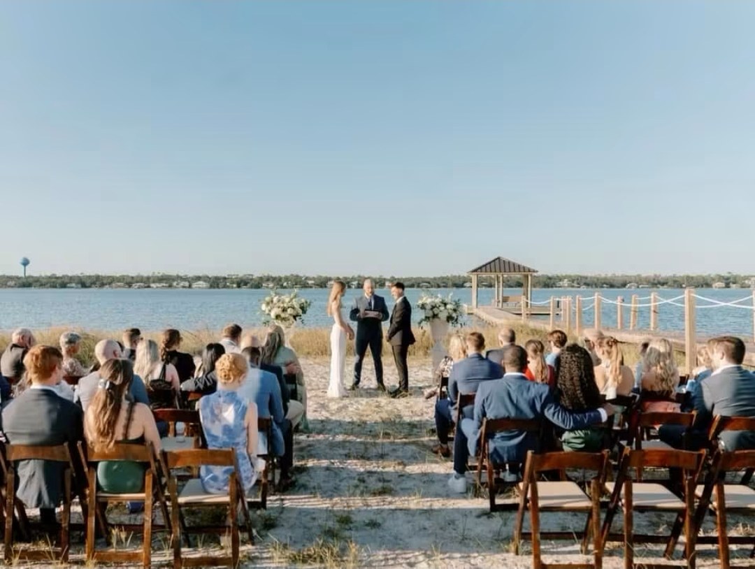 Guests seated on the sand for a ceremony by the water