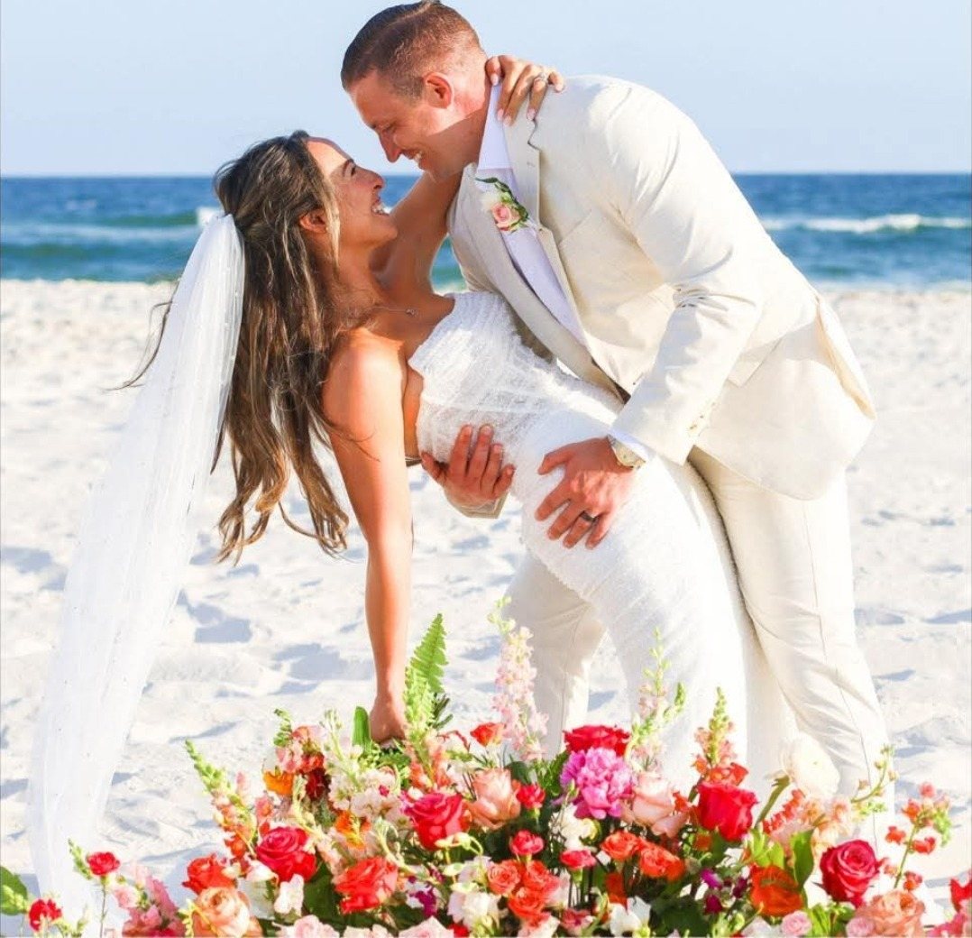 Couple kissing on the beach behind a bank of bright florals