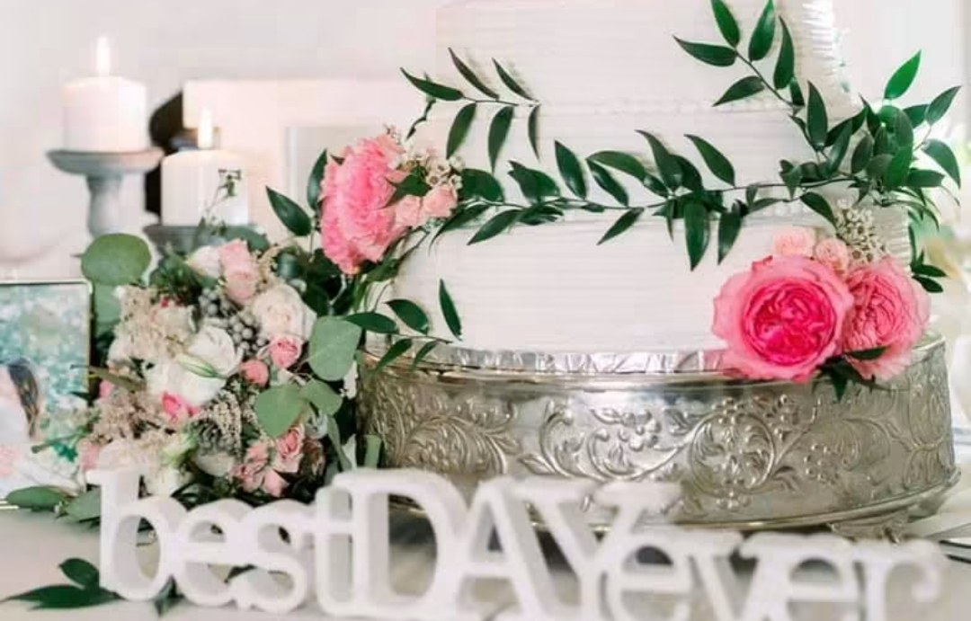 White cake with pink roses and greenery behind a best day ever sign