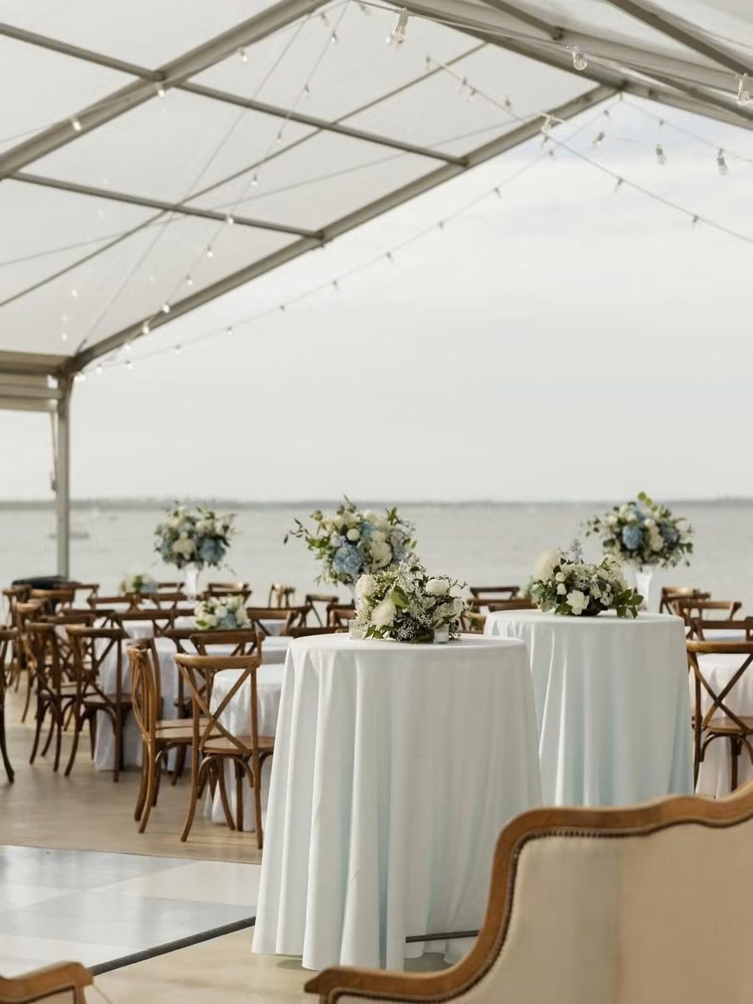 Clear tent reception set with florals, looking out over the water