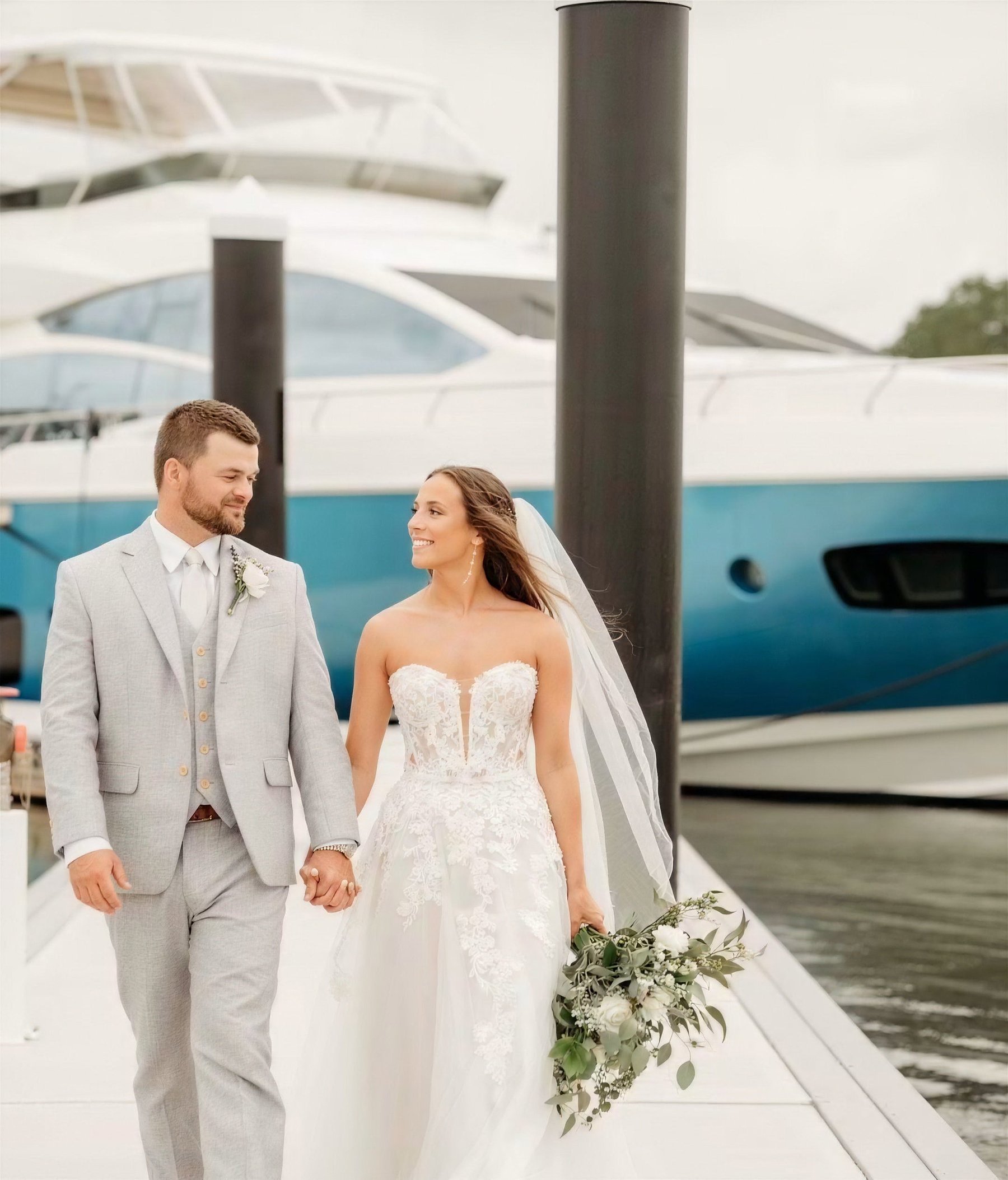 Bride and groom walking hand in hand along a dock beside a yacht