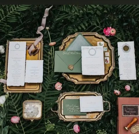 Sage and ivory invitation suite on gold trays among ferns