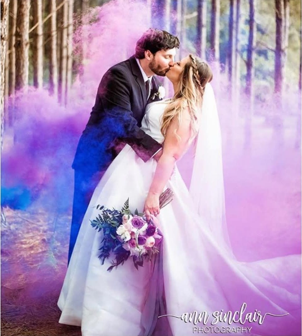 Bride and groom kissing in a pine forest with purple smoke